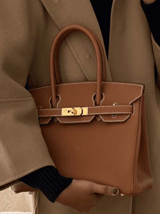 Brown Hermès Birkin carried against a camel coat