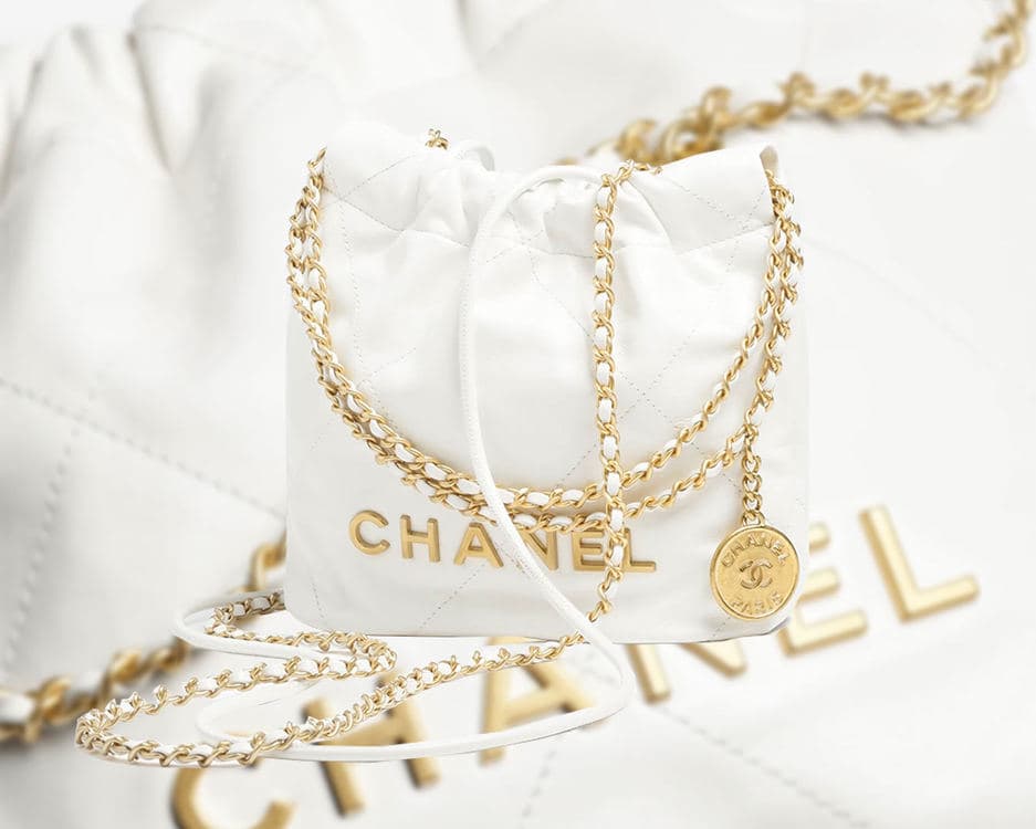 White CHANEL 22 Mini Handbag with gold chains and CHANEL lettering on a quilted white background