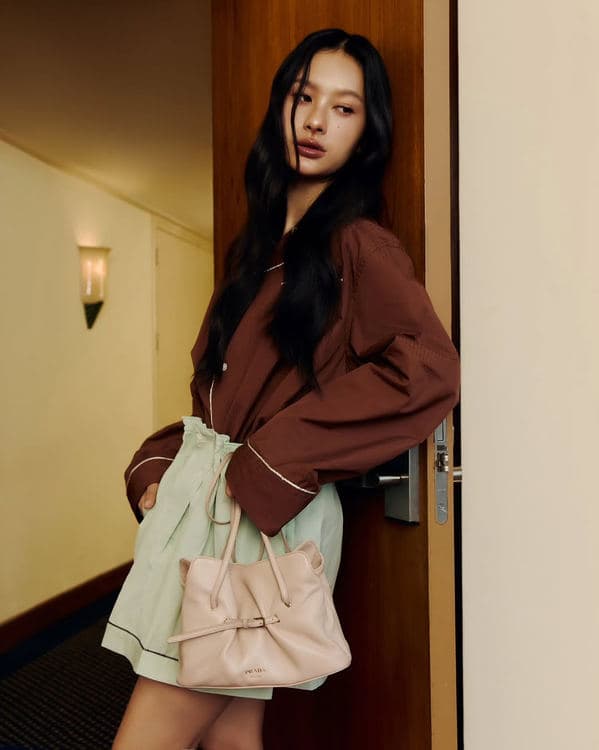 Woman in a rust-coloured blazer holding a beige Prada Dada at her waist
