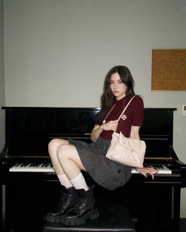 Woman in a burgundy top seated at a piano with a pale pink Prada Dada