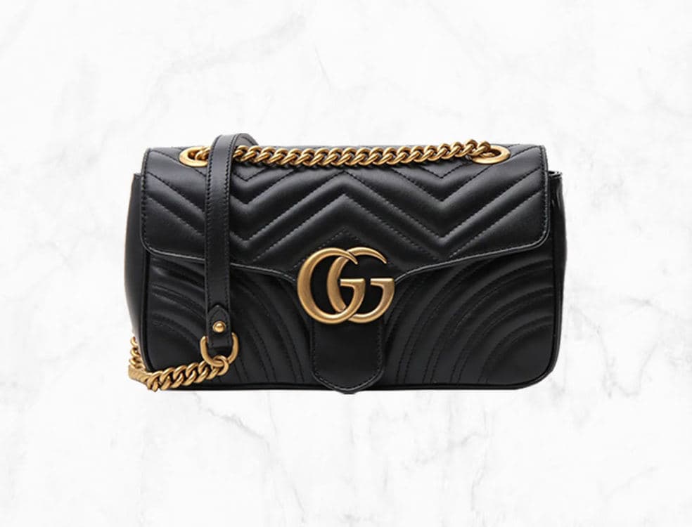 Black quilted leather Gucci GG Marmont bag with gold-tone Double G hardware on a white marble background