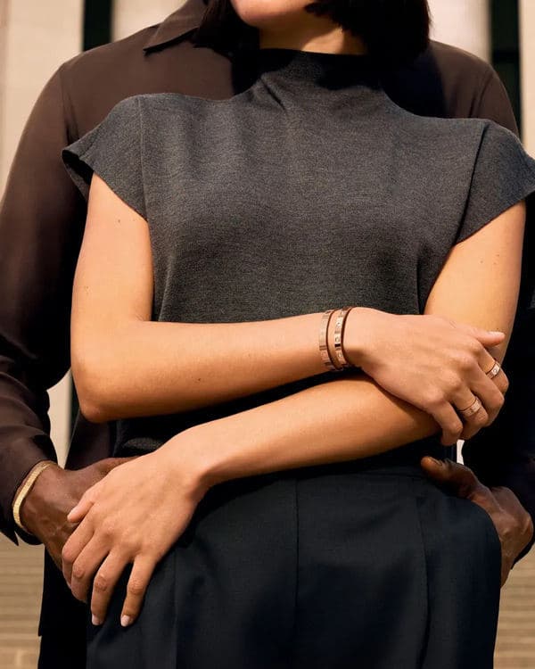 Two people crossing their arms to show stacked Cartier Love Unlimited bracelets