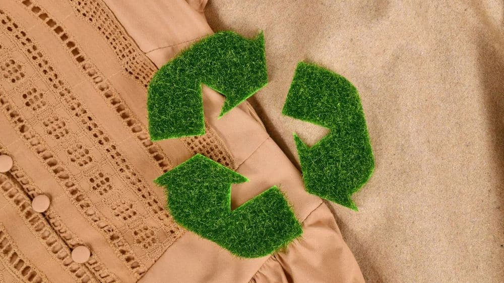 Green recycling symbol arranged over folded beige clothing