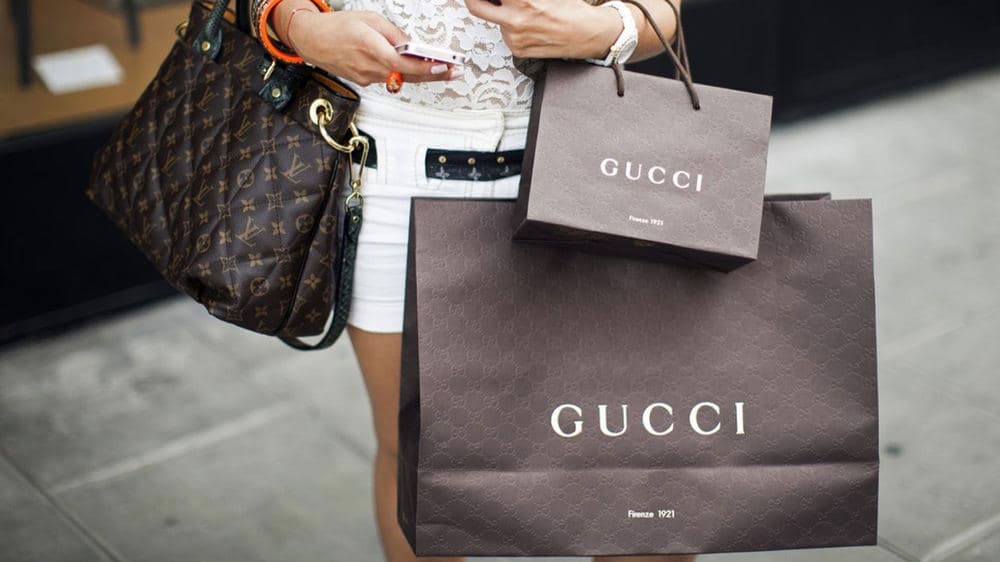 Shopper carrying a Louis Vuitton monogram tote beside Gucci shopping bags