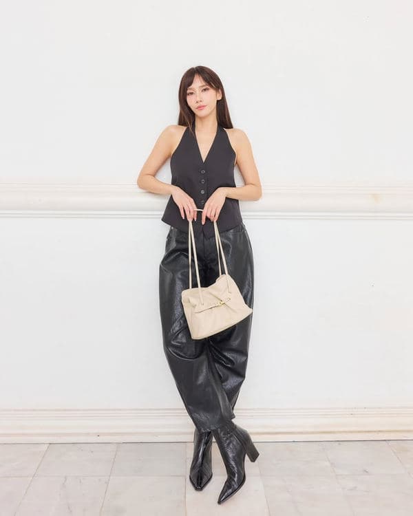 Woman in a black sleeveless outfit holding a cream Prada Dada by its straps