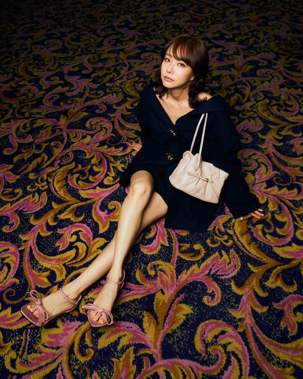 Woman seated on a patterned carpet with a pale Prada Dada and black outfit