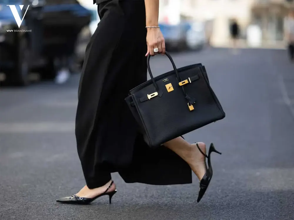 Woman in black carrying a structured black top-handle bag
