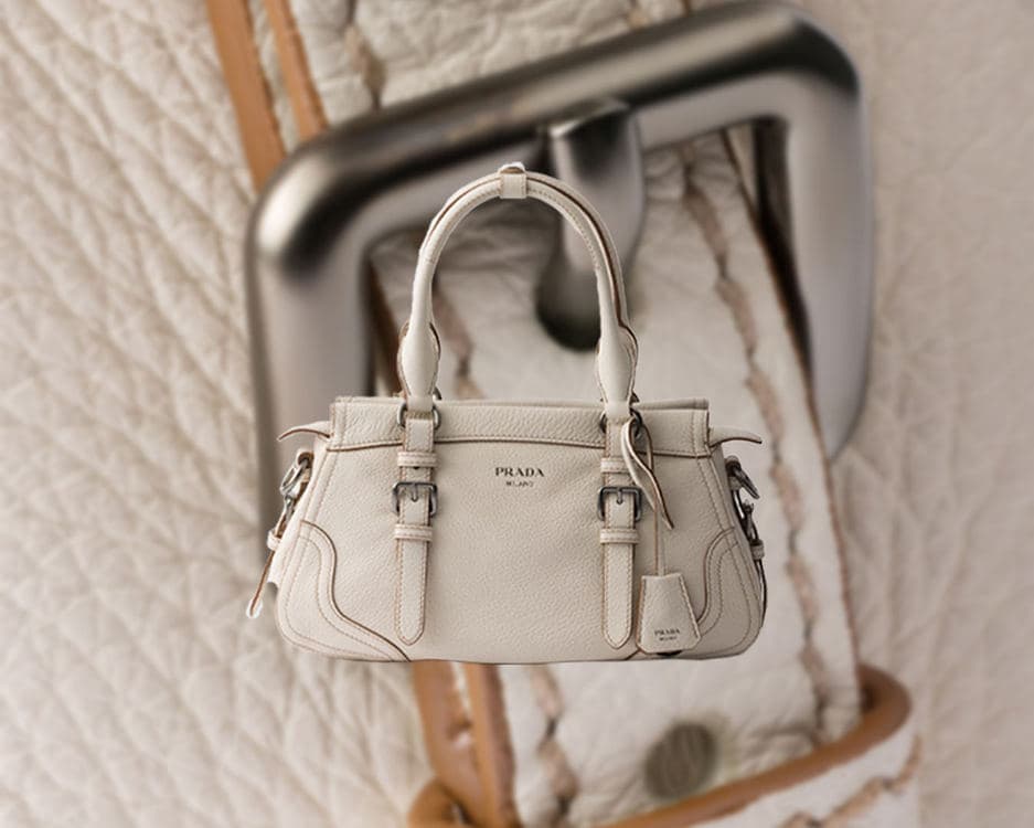 Chalk-white Prada large tote beside stacked travel cases in a three-quarter view