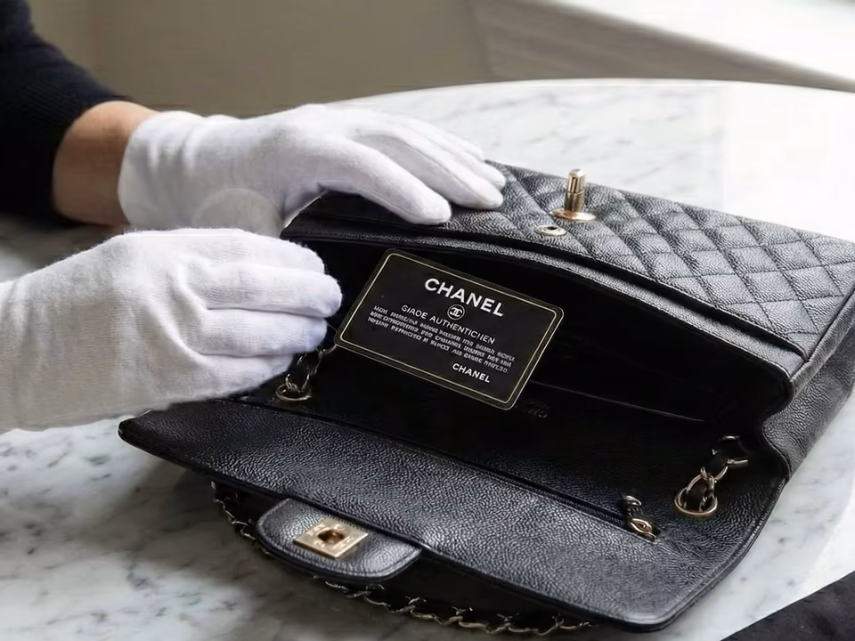 A gloved specialist examining a handbag and its authenticity card