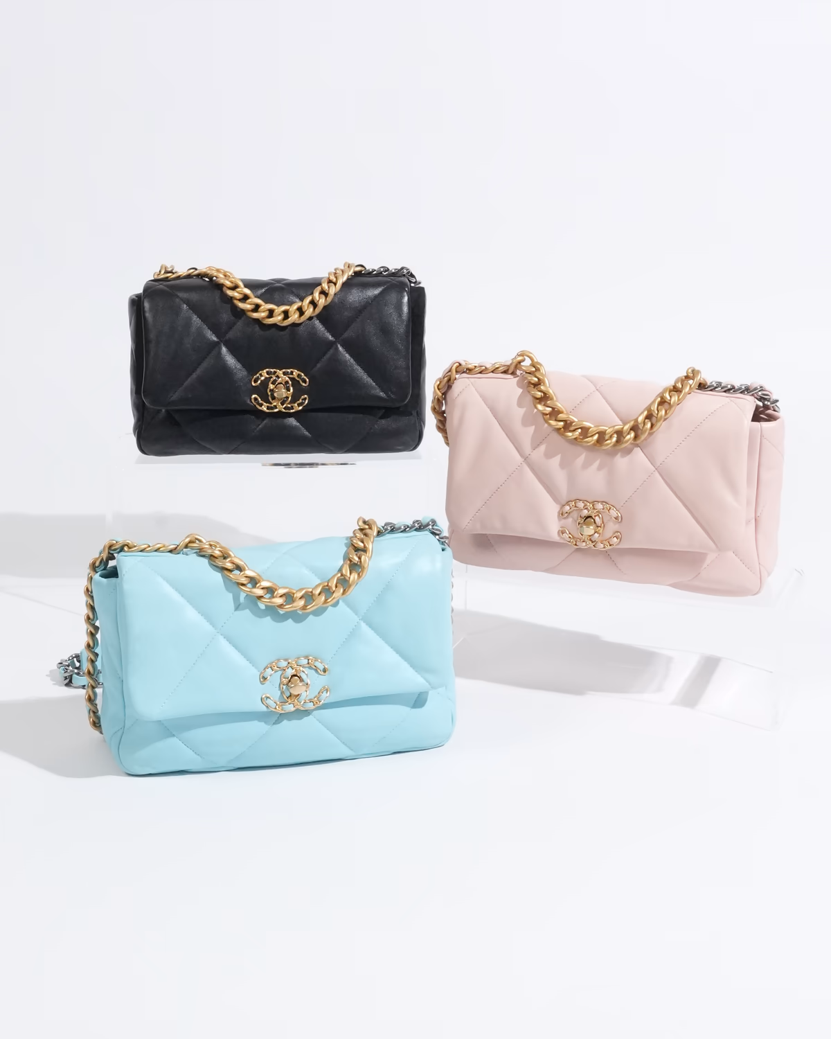 กระเป๋า Chanel สีดำ สีชมพู และสีฟ้า พร้อมสายโซ่ จัดแสดงบนแท่นสีขาว